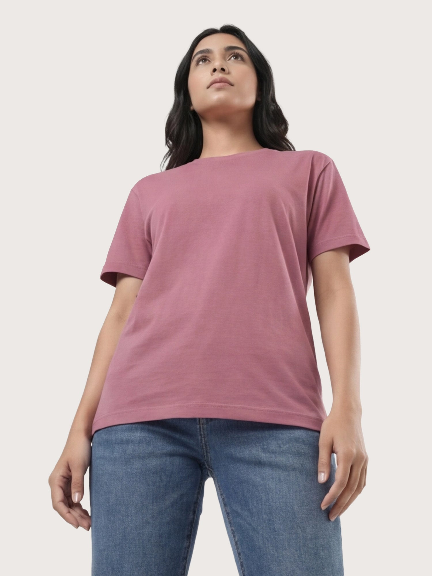 Woman wearing a mauve t-shirt and blue jeans against a light gray background