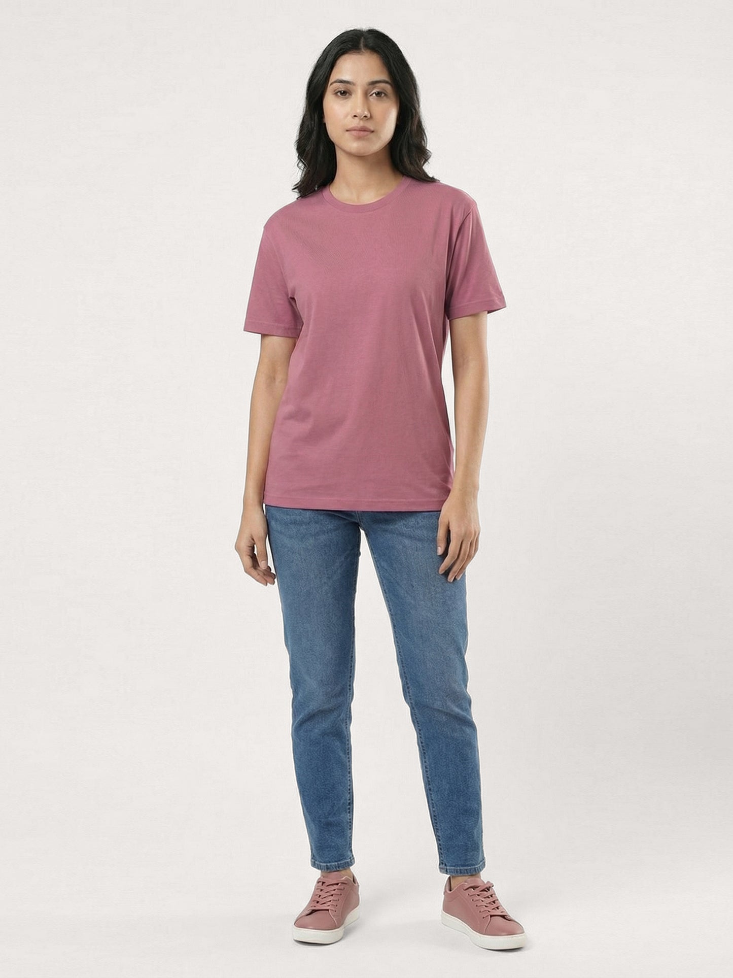 Person wearing a mauve t-shirt and blue jeans on a white background