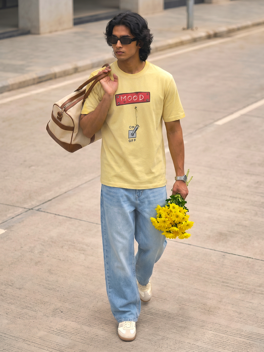 Yellow Mood Graphic T-Shirt Keos yellow graphic t-shirt paired with relaxed light wash denim and white sneakers. A cheerful streetwear look featuring fresh yellow flowers, a duffle bag and effortless city style, blending casual fashion, positive vibes, youth culture and everyday self-expression.

