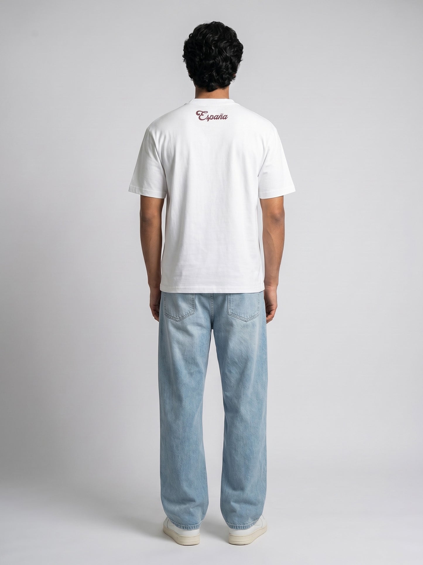 Person wearing a white t-shirt with text on the back and light blue jeans, standing against a plain background