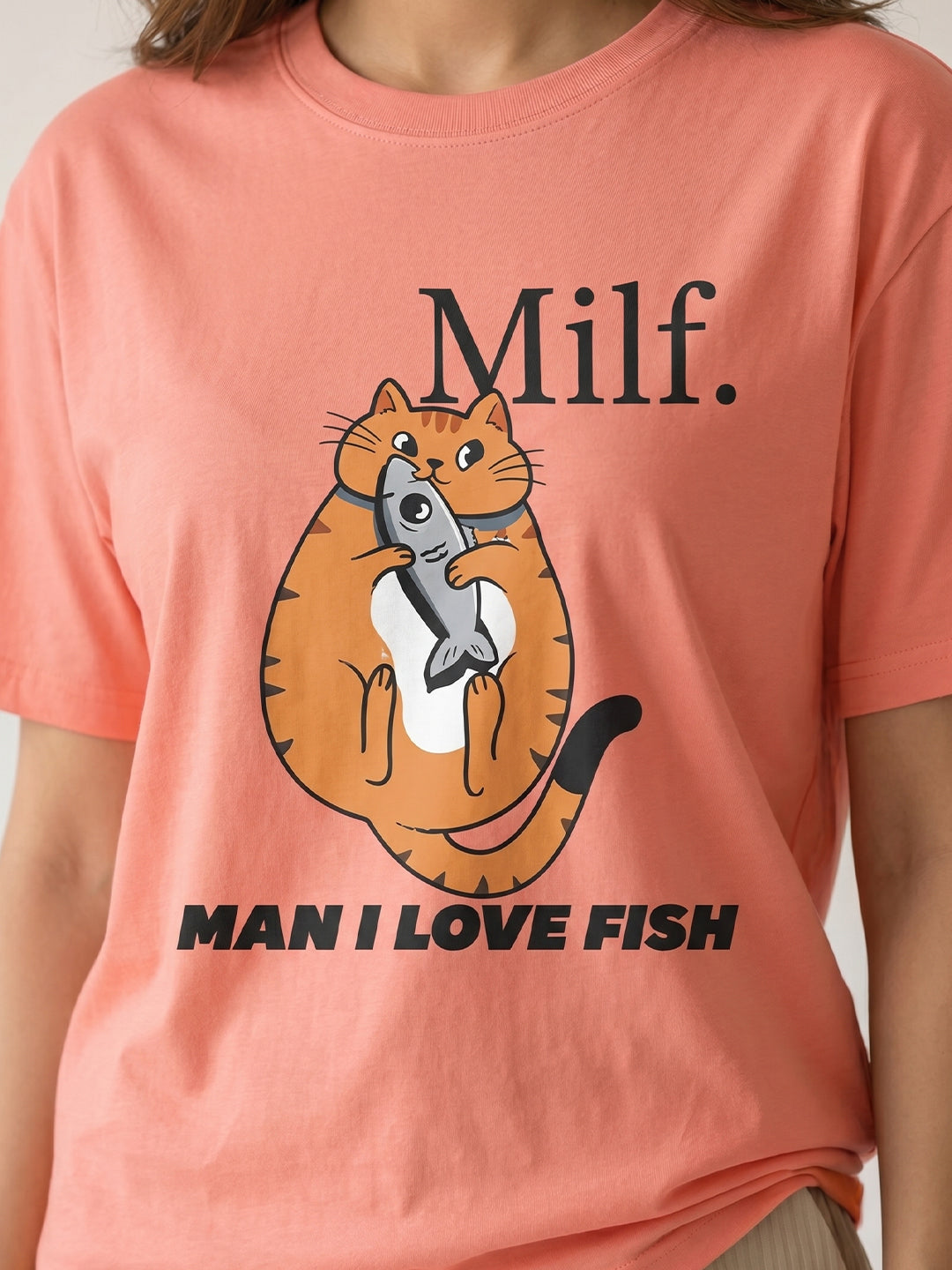 Peach-colored t-shirt with a graphic of a cat holding a fish 