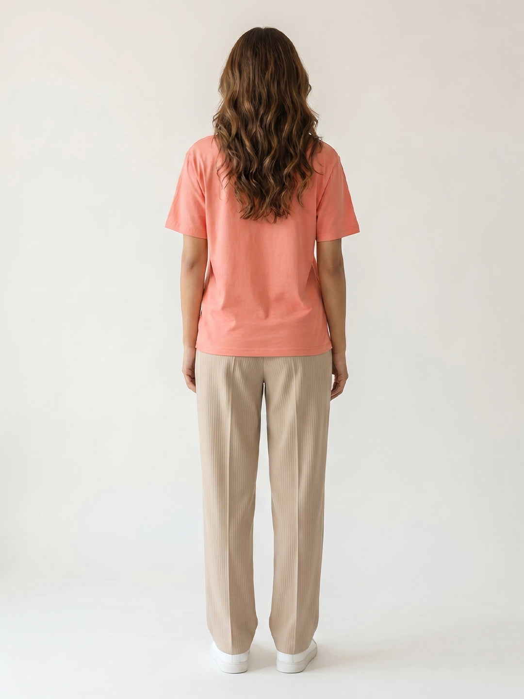 Woman wearing a peach t-shirt and beige pants against a white background